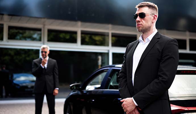 Professional executive protection security personnel providing close protection outside luxury vehicle and commercial property