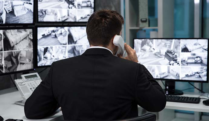 Security officer using a walkie-talkie while monitoring multiple surveillance camera screens showing different property areas